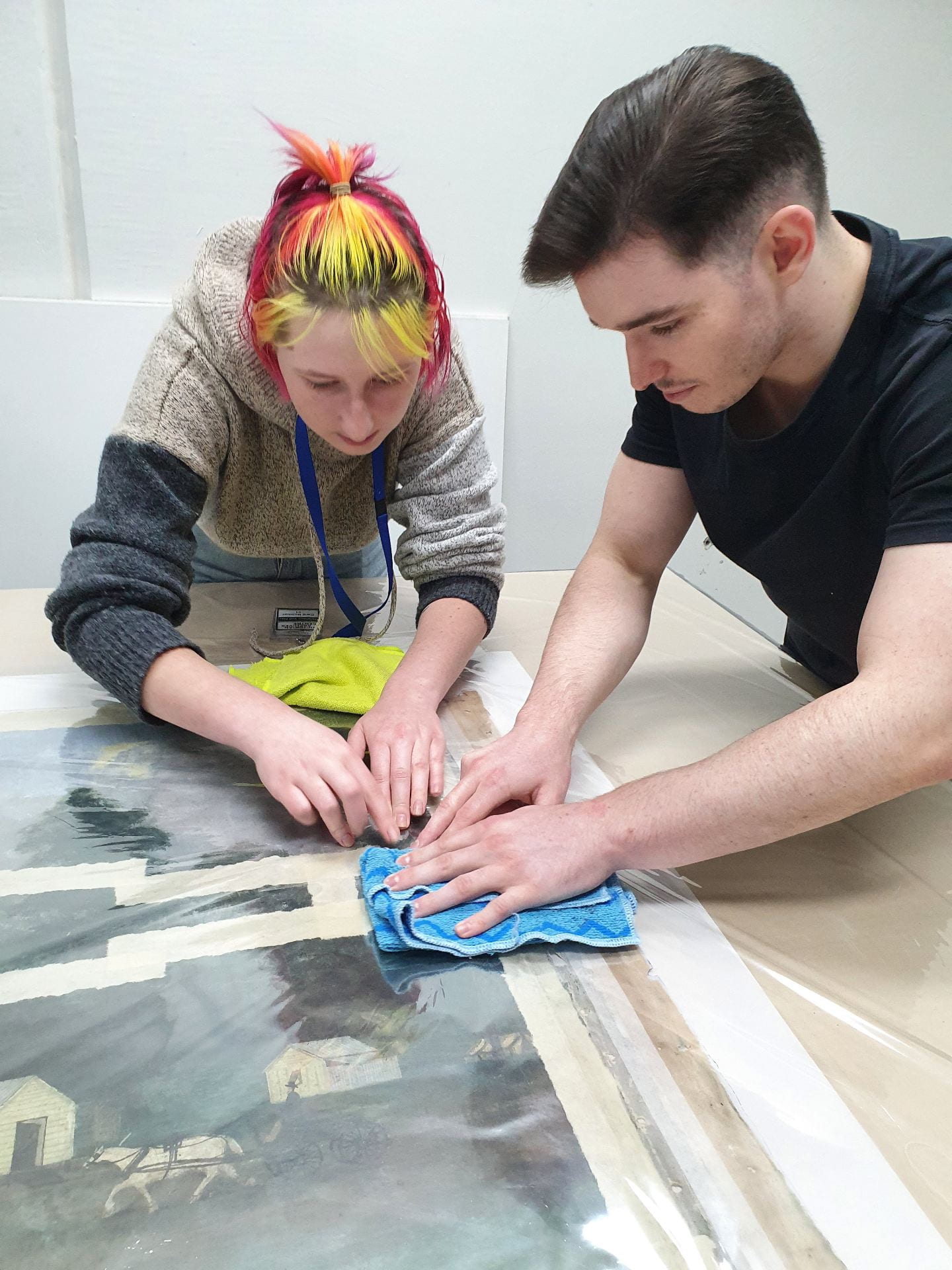 Two students pressing on a painting on a table