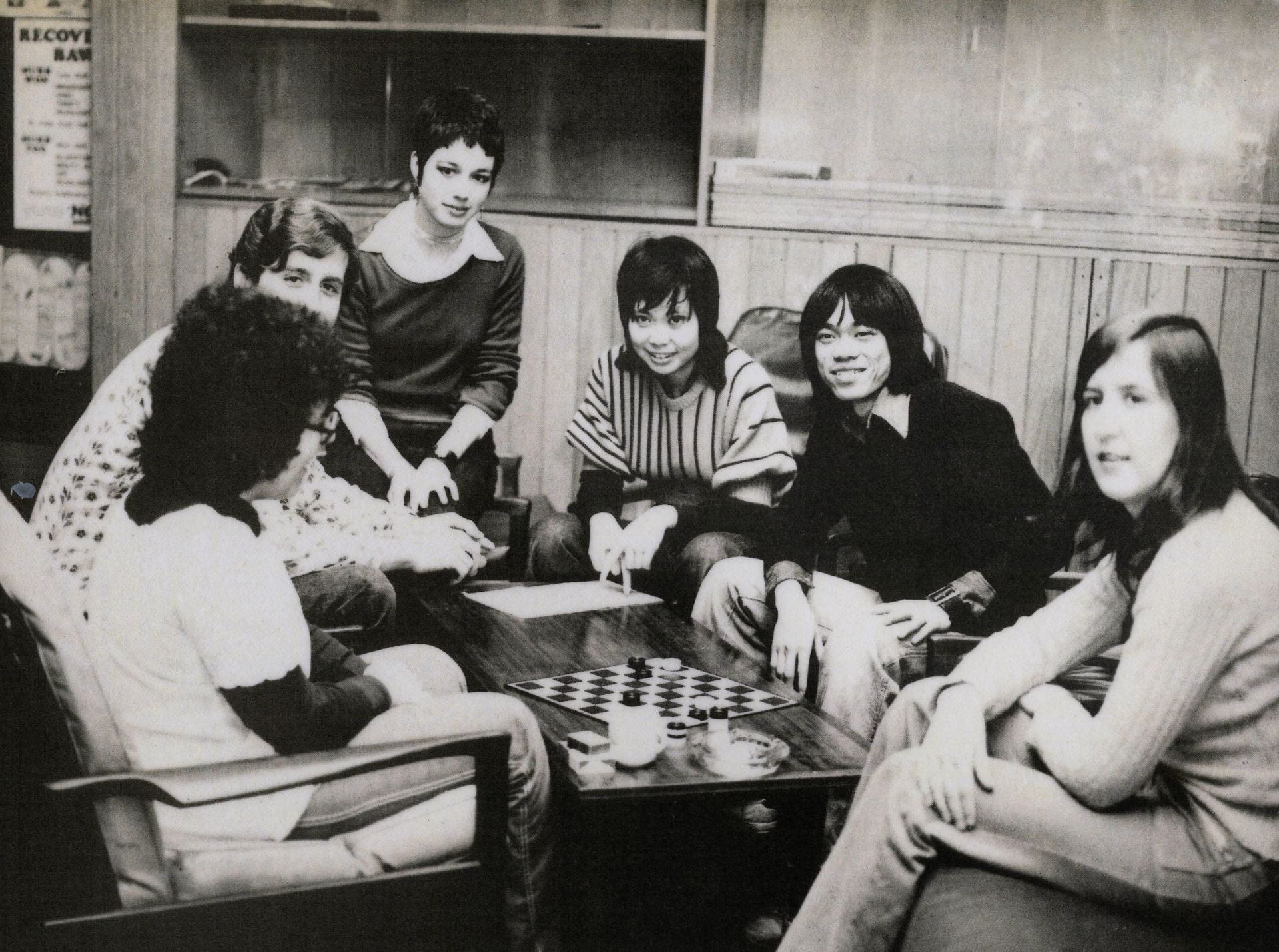 Black and white photograph of a group of male and students gathered around a chess board in the early 1970s.