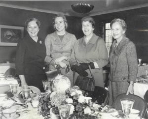 Black and white photograph of four women, including Lady Alice Paton, standing in front of a table set for a formal dinner.