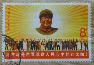 Stamp depicting Chairman Mao's head and shoulders in the middle of the sun, floating over a crowd of people.