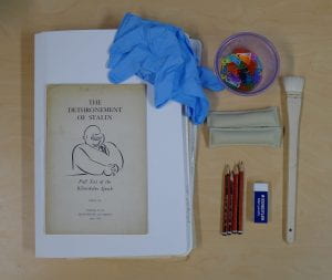 Flat lay of archival processing equipment with ‘The Dethronement of Stalin: Full Text of the Khrushchev Speech’. Includes brushes, pencils, erasers, blue gloves and paperclips.