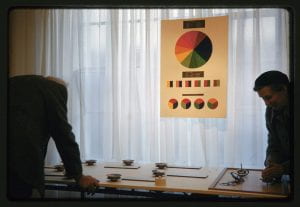 Colour photograph of two people looking at a table with various spinning tops. Above the table hangs a colour chart and a colour chart explaining how the spinning tops work.