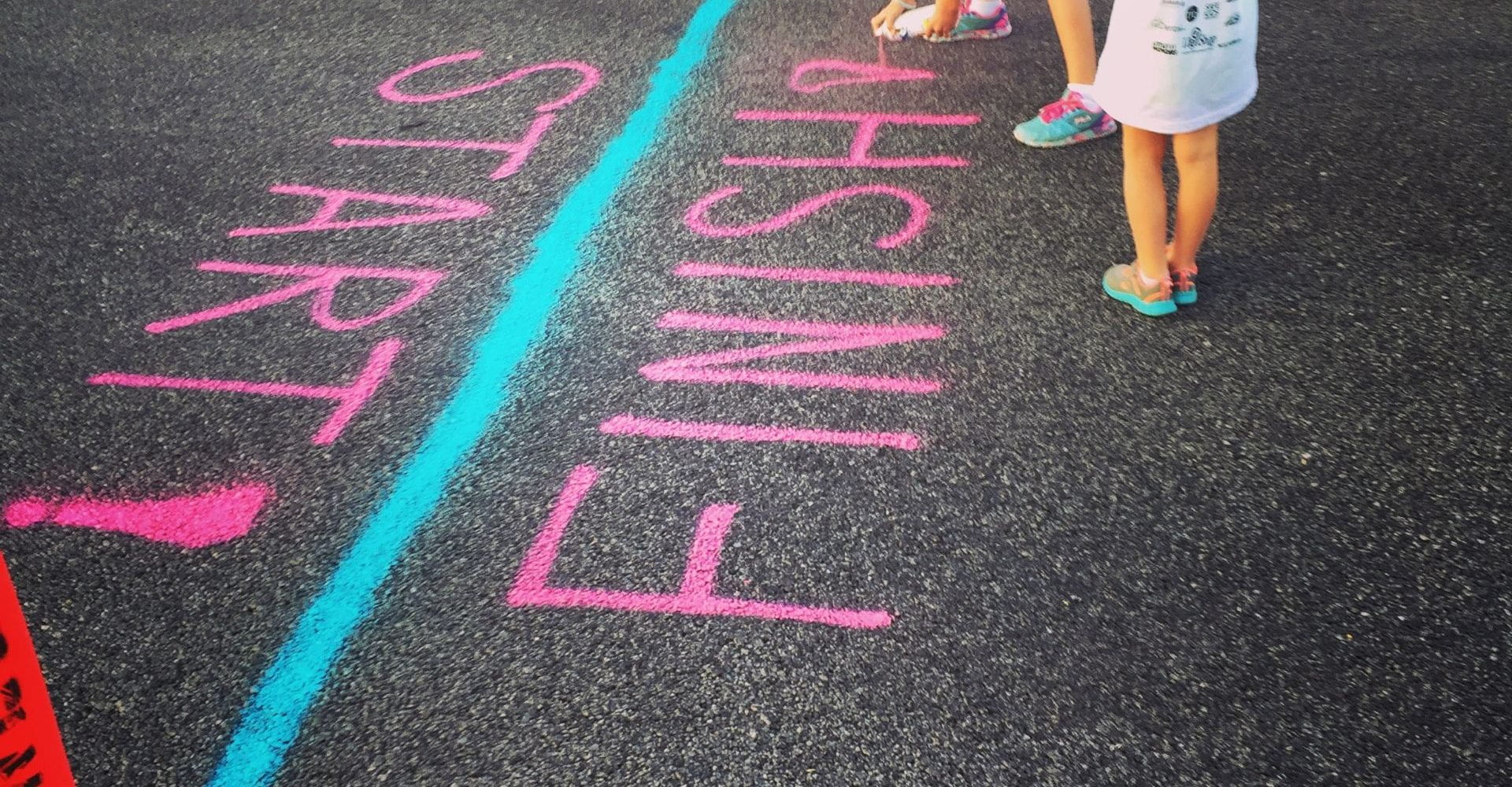 Two children drawing 'start' and 'finish' on the concrete in chalk