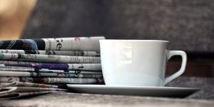 A stack of newspapers next to a coffee cup.