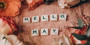A pink blanket with scrabble tiles spelling out "Hello May." The scrabble tiles are surrounded by orange, pink and white flowers.